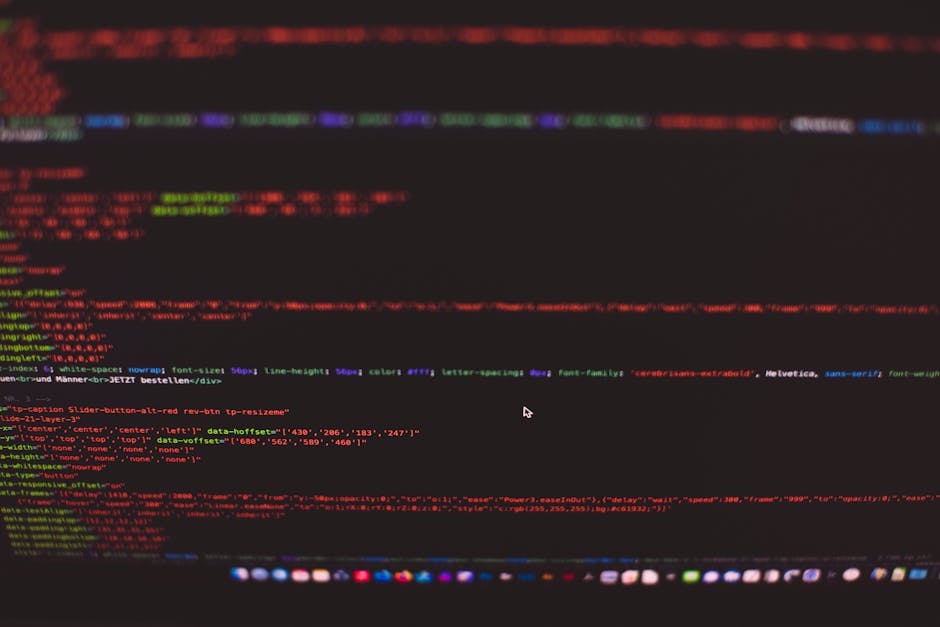 A person wearing a wristwatch is using a laptop on a wooden desk, focusing on a screen displaying lines of code with colorful syntax highlighting. The person's hand is positioned over the keyboard, fi
